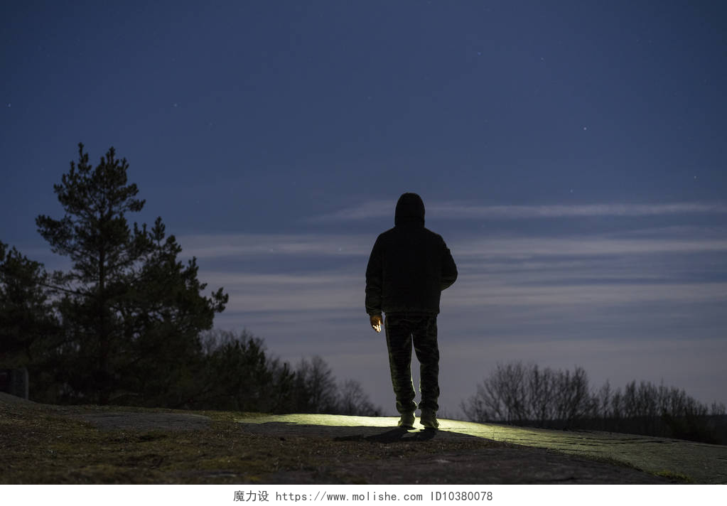 一个男人打着手电筒走在户外男子站在户外在夜间森林闪耀着手电筒